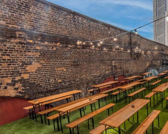 The rooftop terrace — long benches on grass under festoon lights against a brick wall